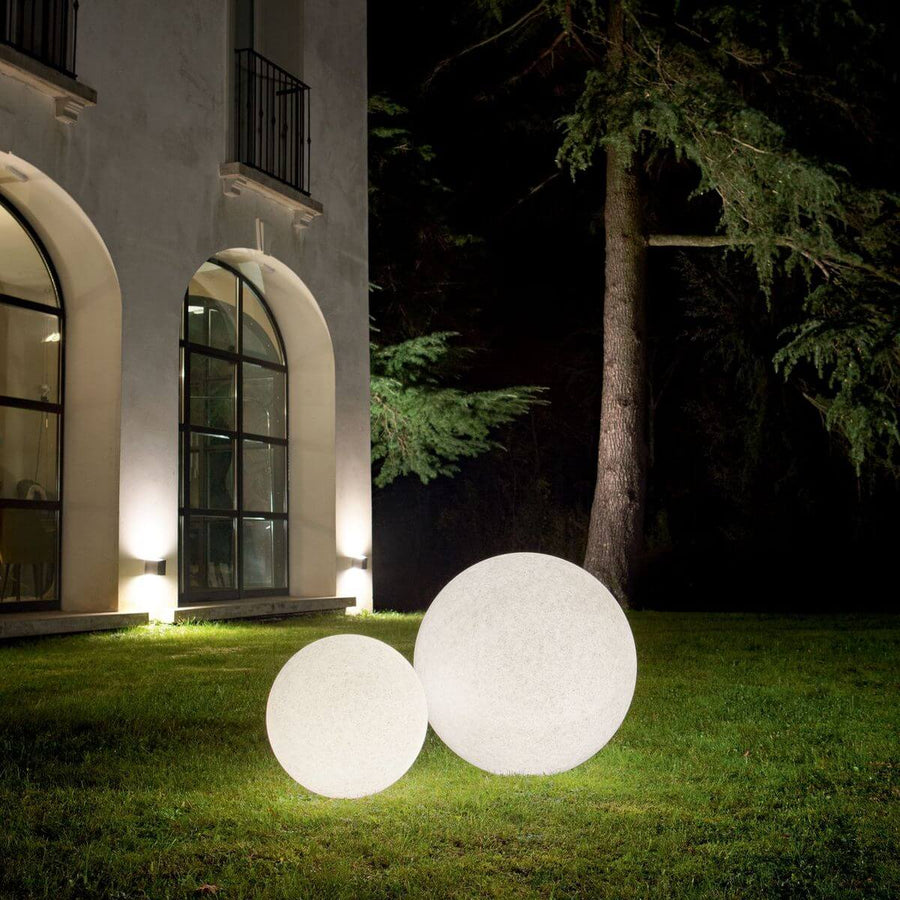 Deux sphères lumineuses blanches posées sur la pelouse devant une maison la nuit.
