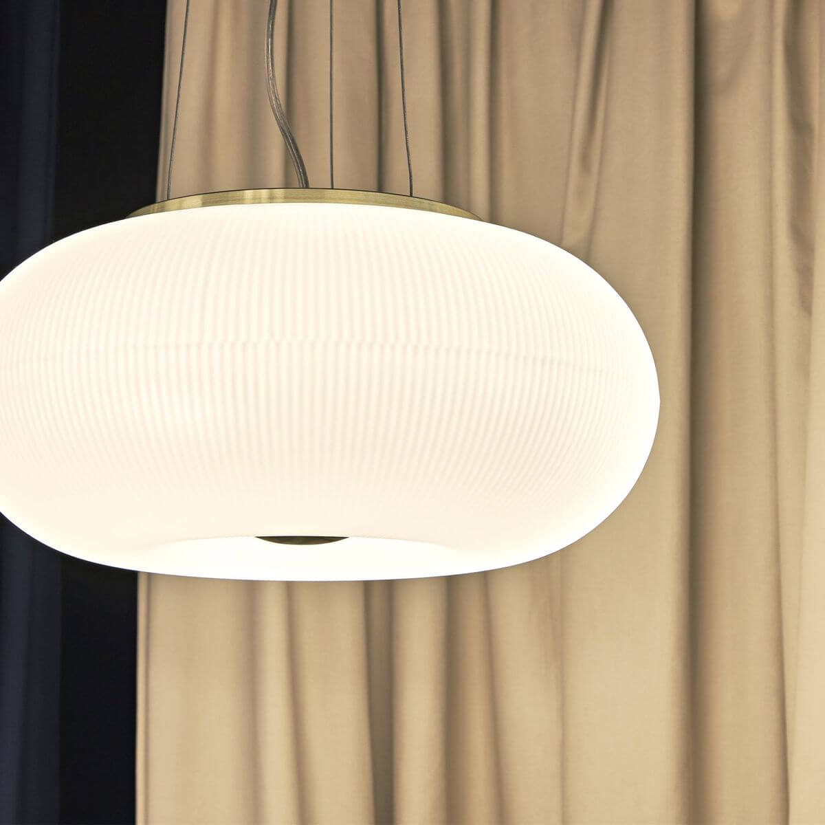 Suspension présentée devant des rideaux beiges, éclairée et vue de face.