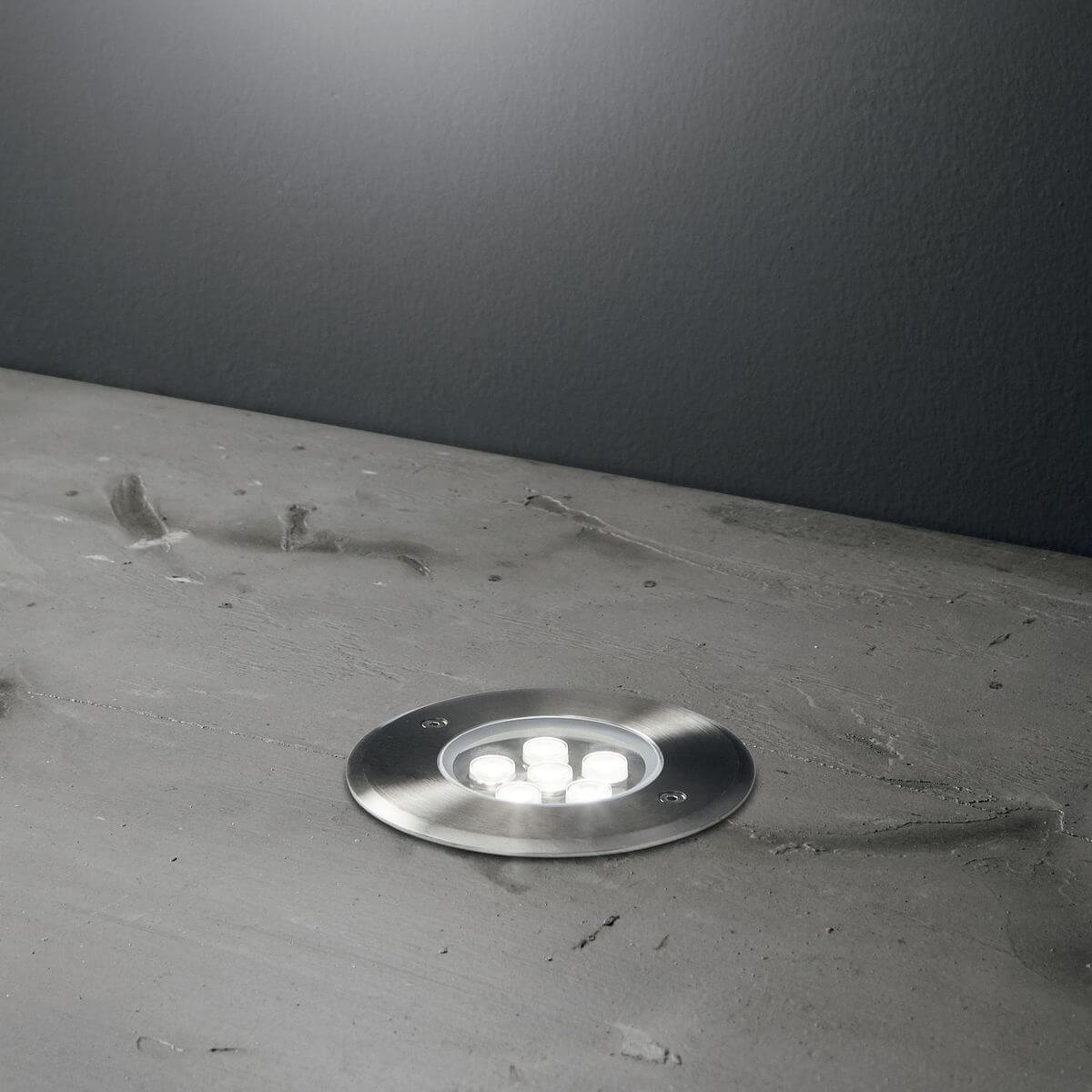 Spot encastré au sol dans du béton, allumé, éclairant la surface grise.