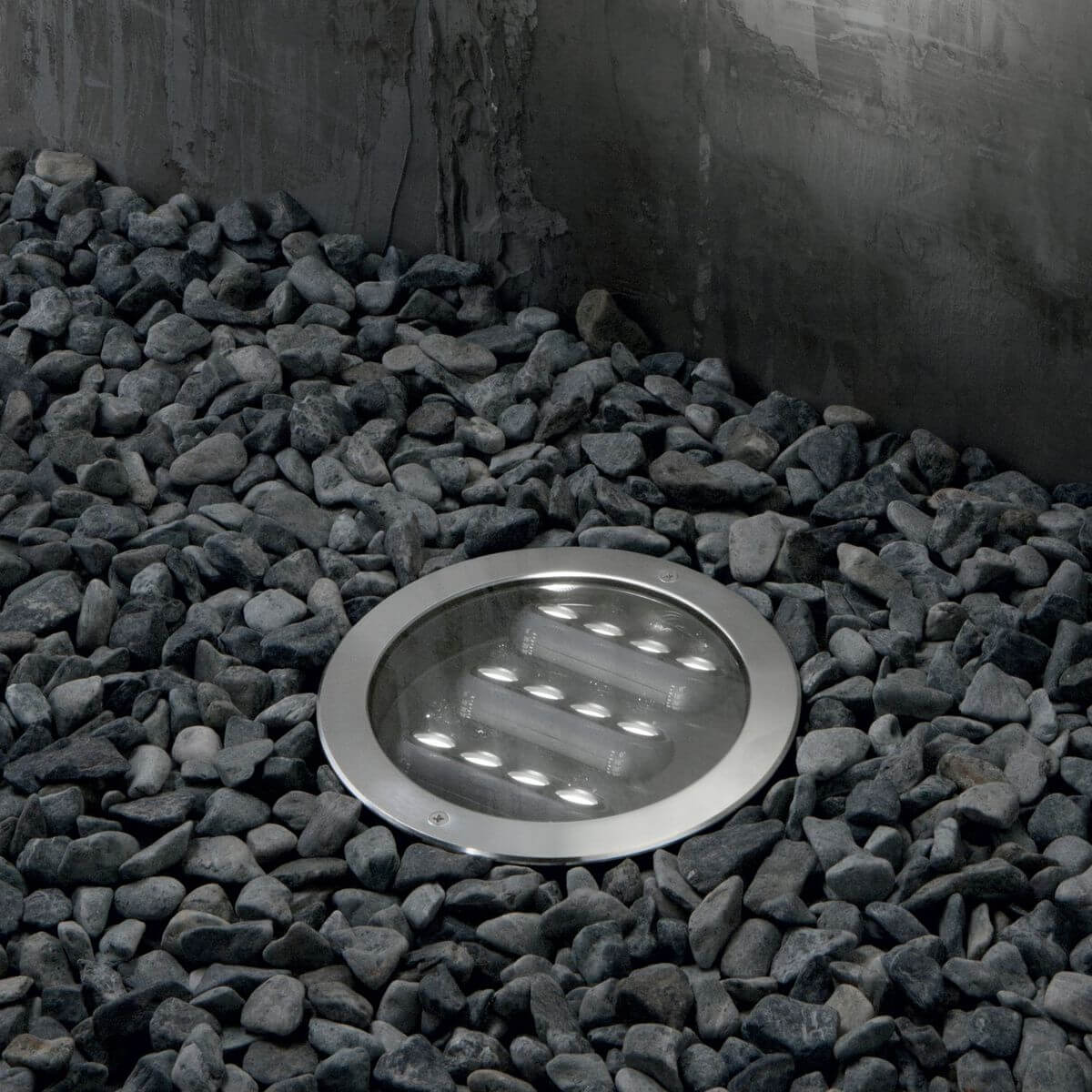 Luminaire encastré dans un lit de galets gris, éclairé et vu de face