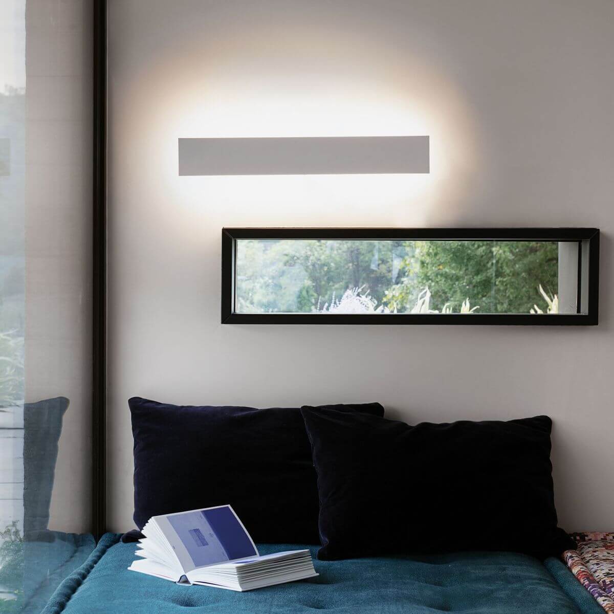 Mise en ambiance : applique allumée au-dessus d'un lit, halo lumineux sur le mur
