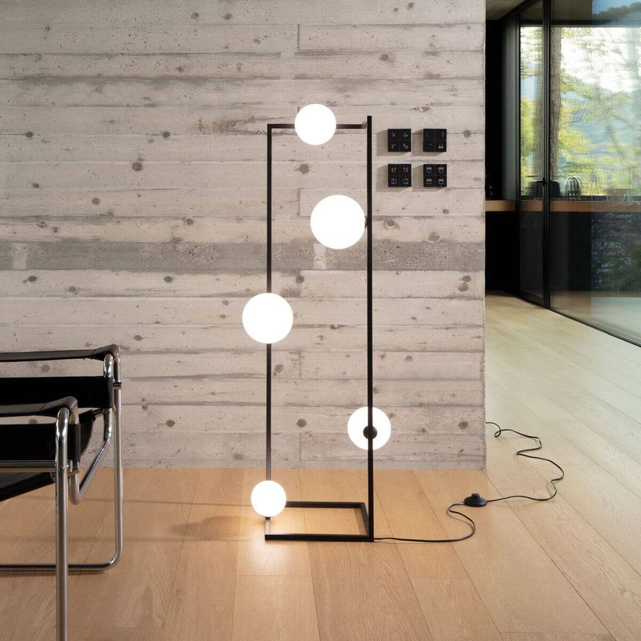Lampadaire posé dans un intérieur béton près d'un fauteuil, câble et interrupteur visibles