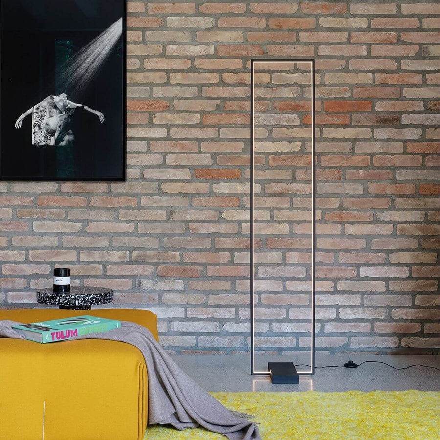 Lampadaire allumé devant un mur de briques dans un salon avec canapé jaune.