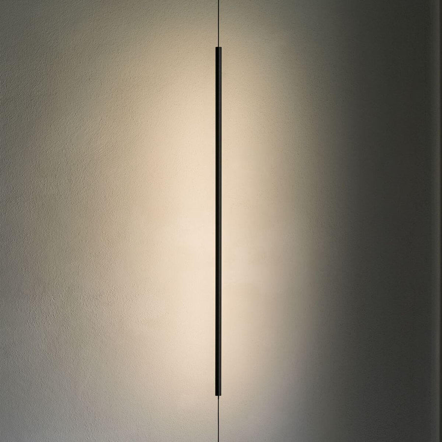 Le tube noir allumé projette un halo de lumière chaude sur un mur texturé