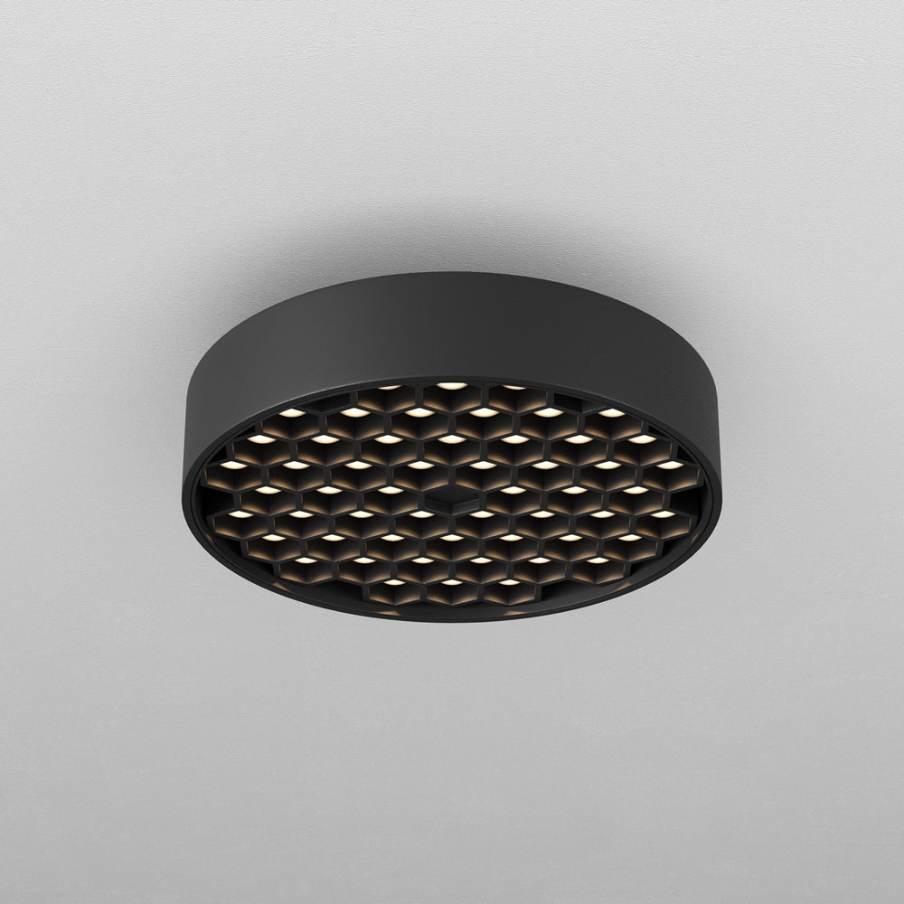 Vue de dessous d'un luminaire rond noir avec grille alvéolée allumée.