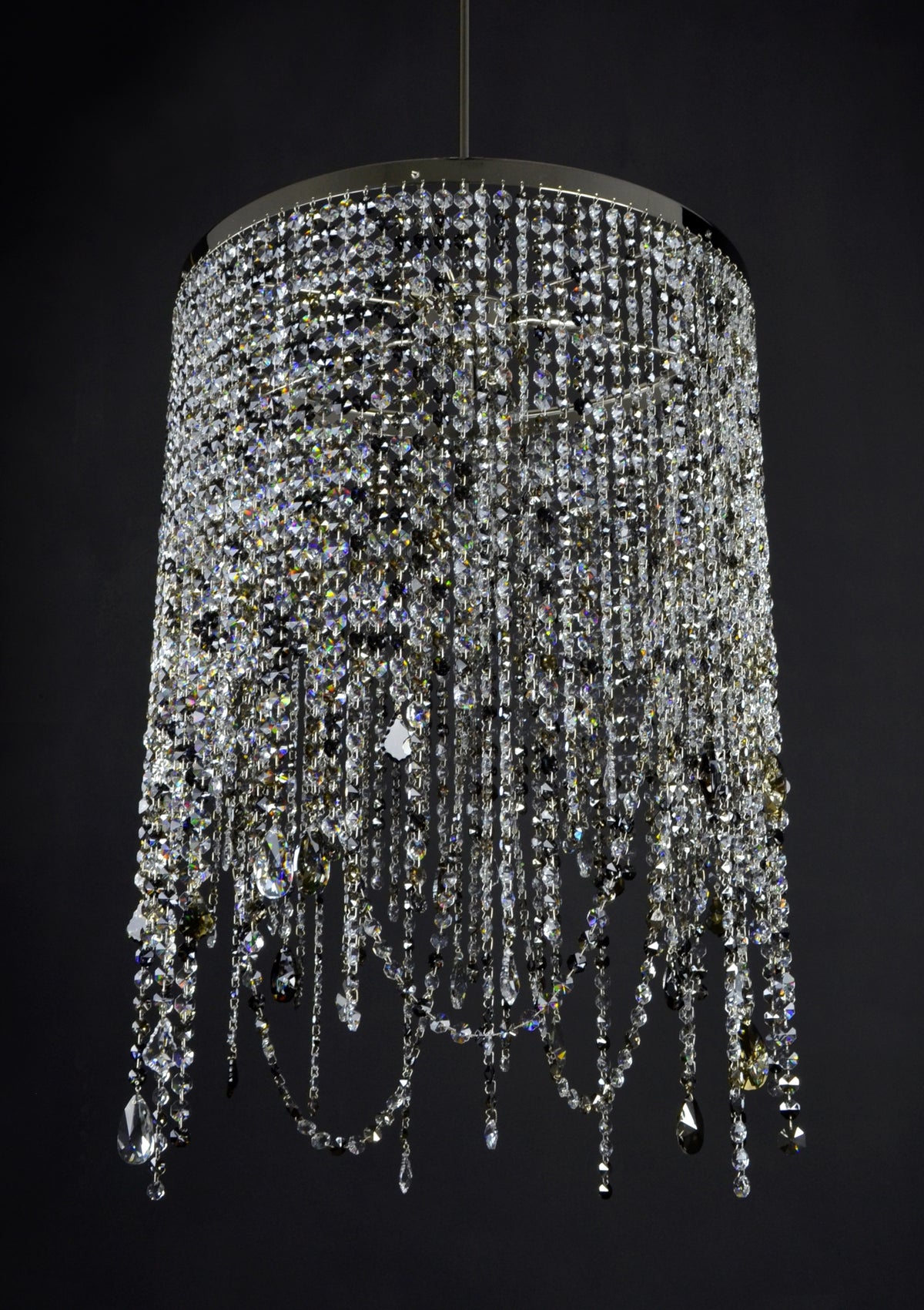 Lustre cylindrique à cascades de cristaux taillés, suspendu sur fond noir, vue rapprochée.