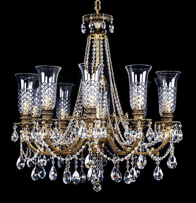 Lustre doré à bras multiples, suspensions en cristal taillé, vue de face sur fond noir.