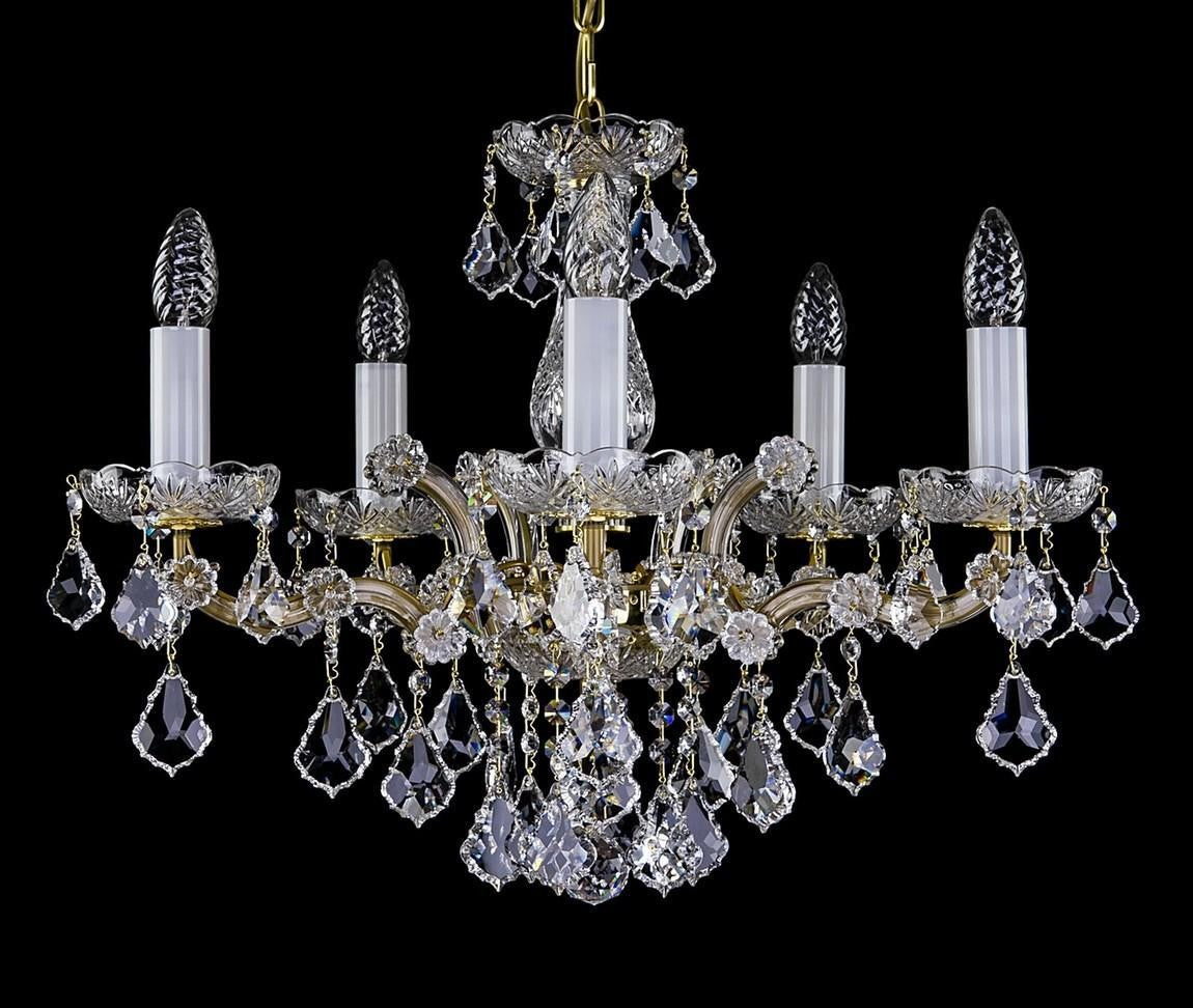 Lustre cinq branches en cristal, monture dorée, pendeloques et bobèches taillées sur fond noir.