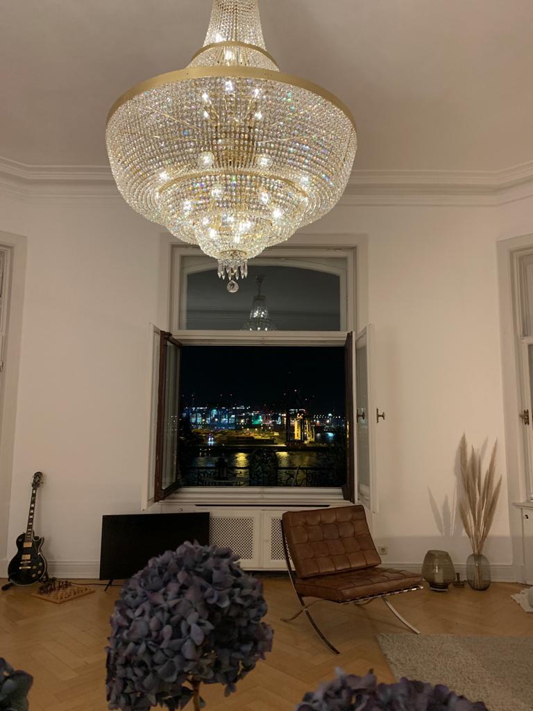 Gros plan du lustre suspendu devant une fenêtre ouverte sur la ville nocturne.