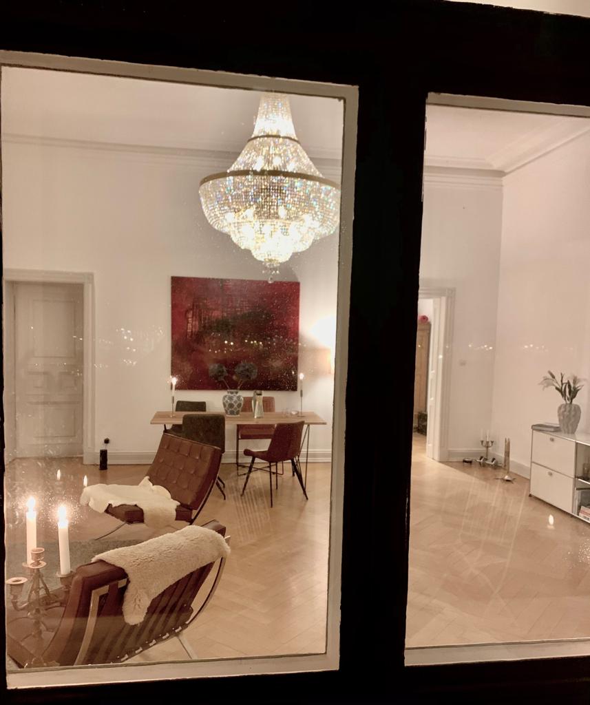 Reflet du lustre dans une fenêtre la nuit, intérieur avec table et fauteuils.