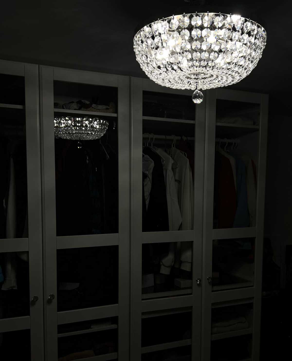 Luminaire illuminé dans une pièce sombre, devant une grande armoire vitrée.