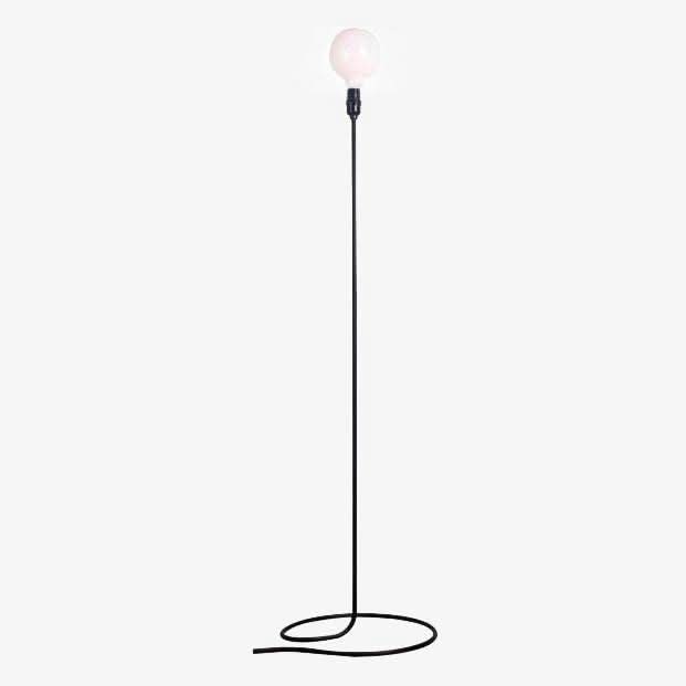 Lampadaire minimaliste noir debout, ampoule globe blanche allumée, câble enroulé formant socle au sol