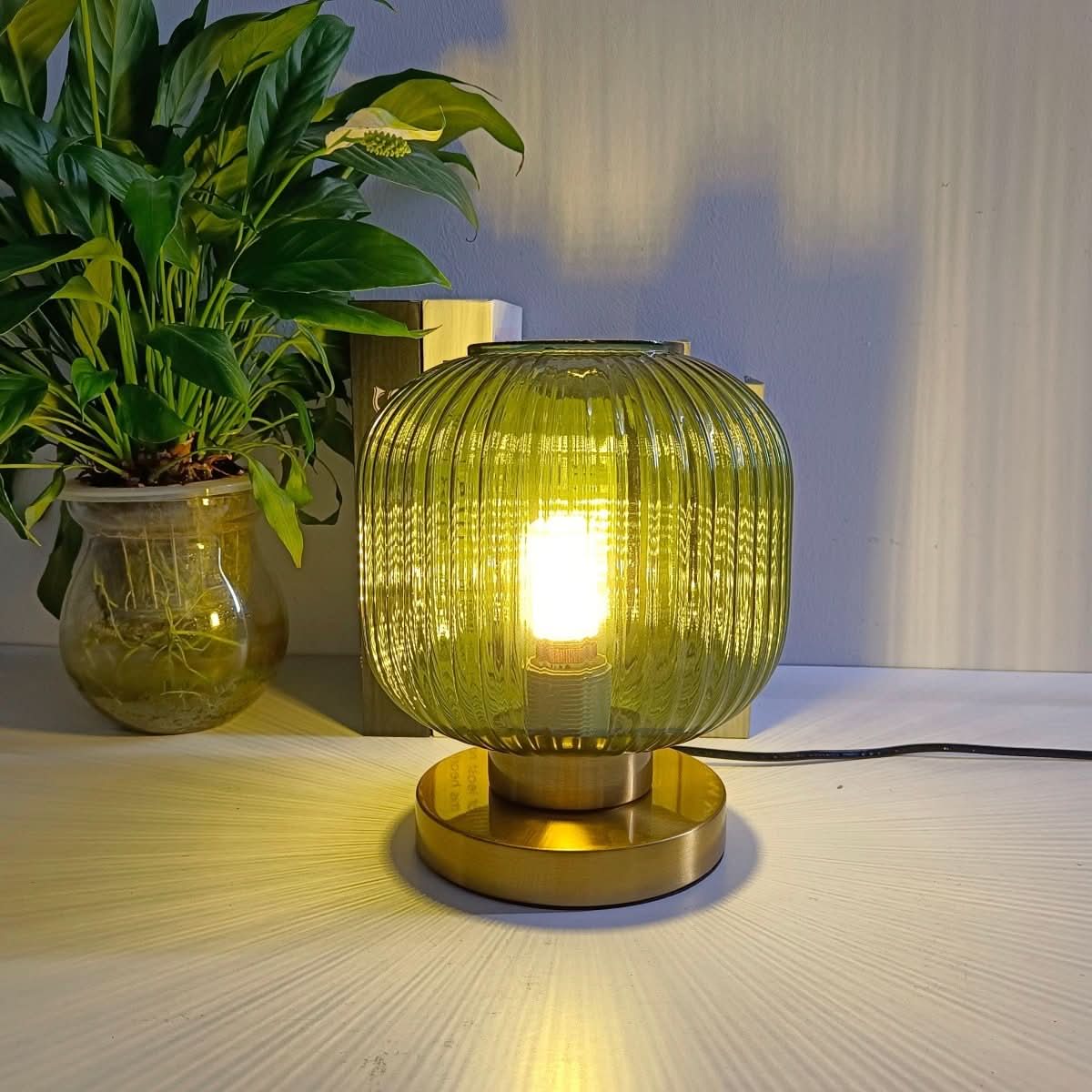 Lampe à poser en verre strié vert jaune, base dorée, posée sur table blanche