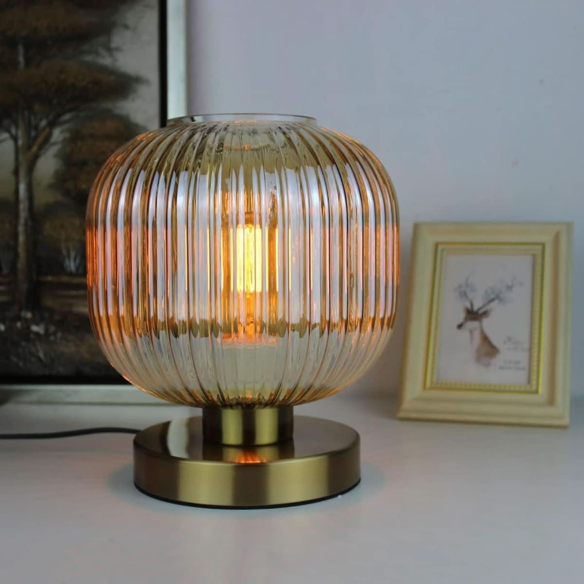 Lampe à poser en verre ambré et laiton brossé, près d'un cadre doré