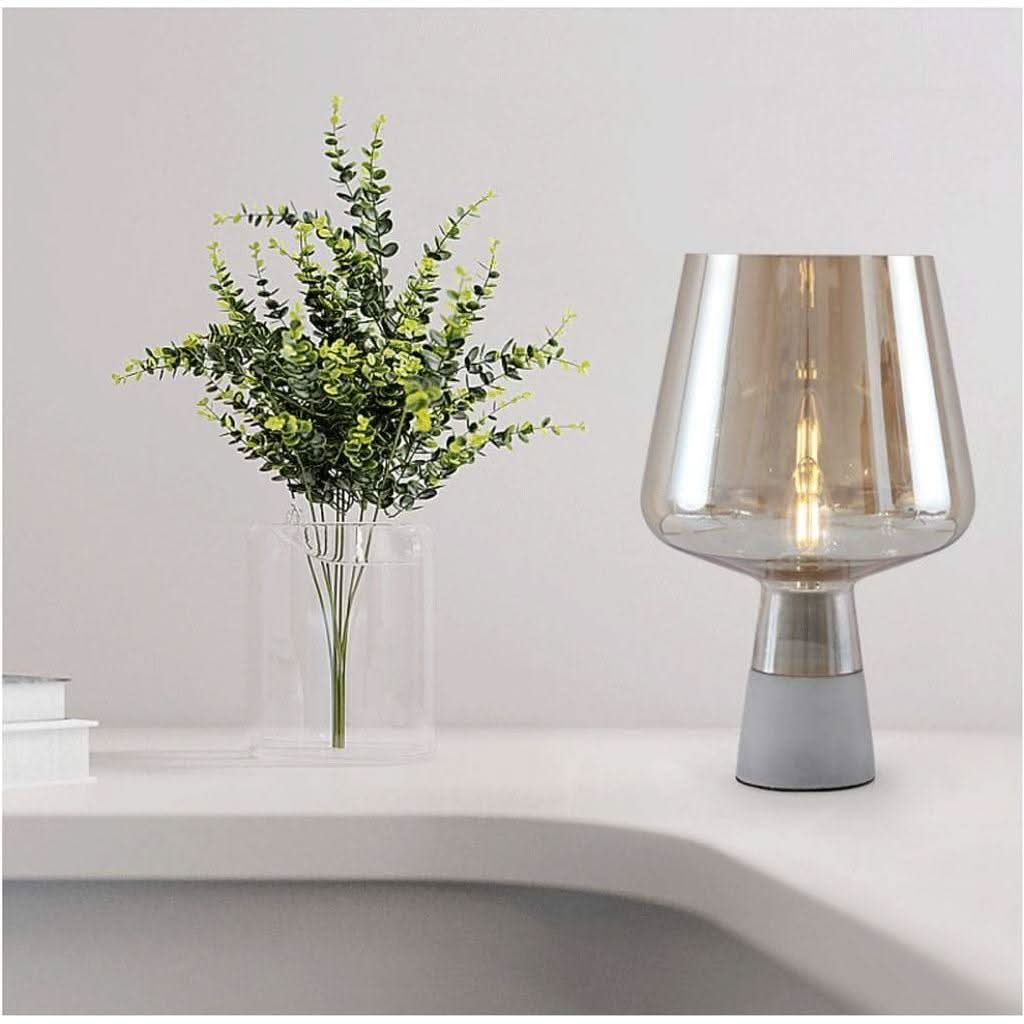 Lampe à poser en verre fumé posée sur une étagère blanche près d'un vase d'eucalyptus.