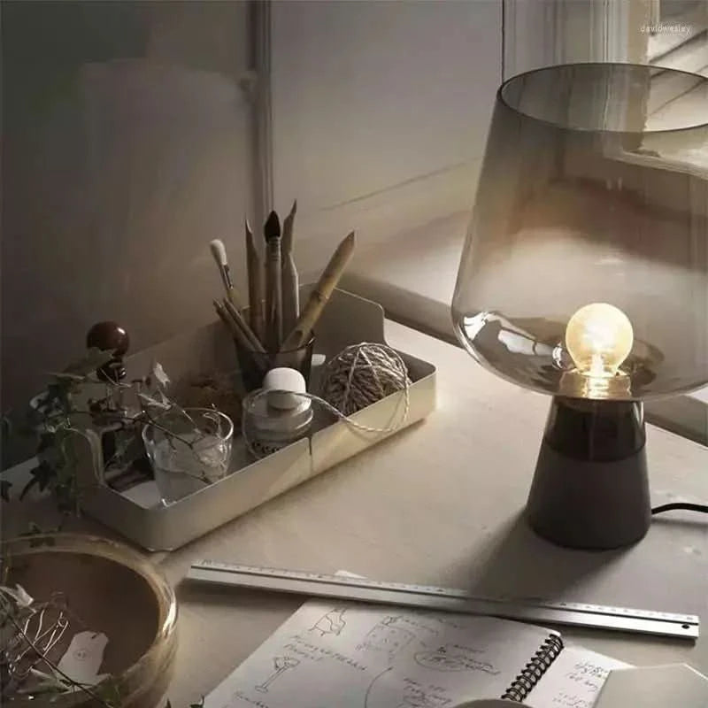 Lampe à poser allumée sur un bureau créatif, entourée de pinceaux, carnet et règle.