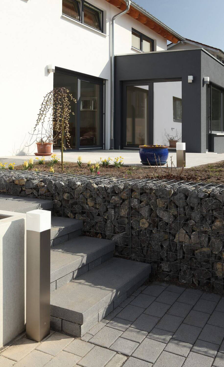 Plan rapproché sur une terrasse avec deux bornes en inox et un mur en gabions.