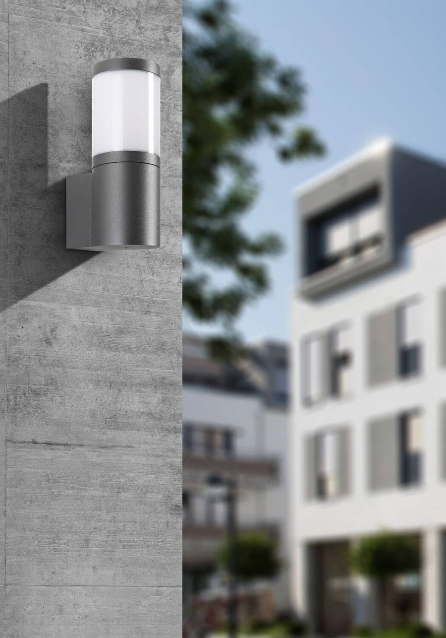 Gros plan de l'applique murale anthracite sur mur béton, arrière-plan urbain flou.