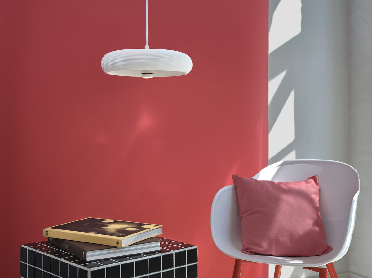 Mise en ambiance dans un intérieur moderne, mur rouge, fauteuil blanc et coussin rose.
