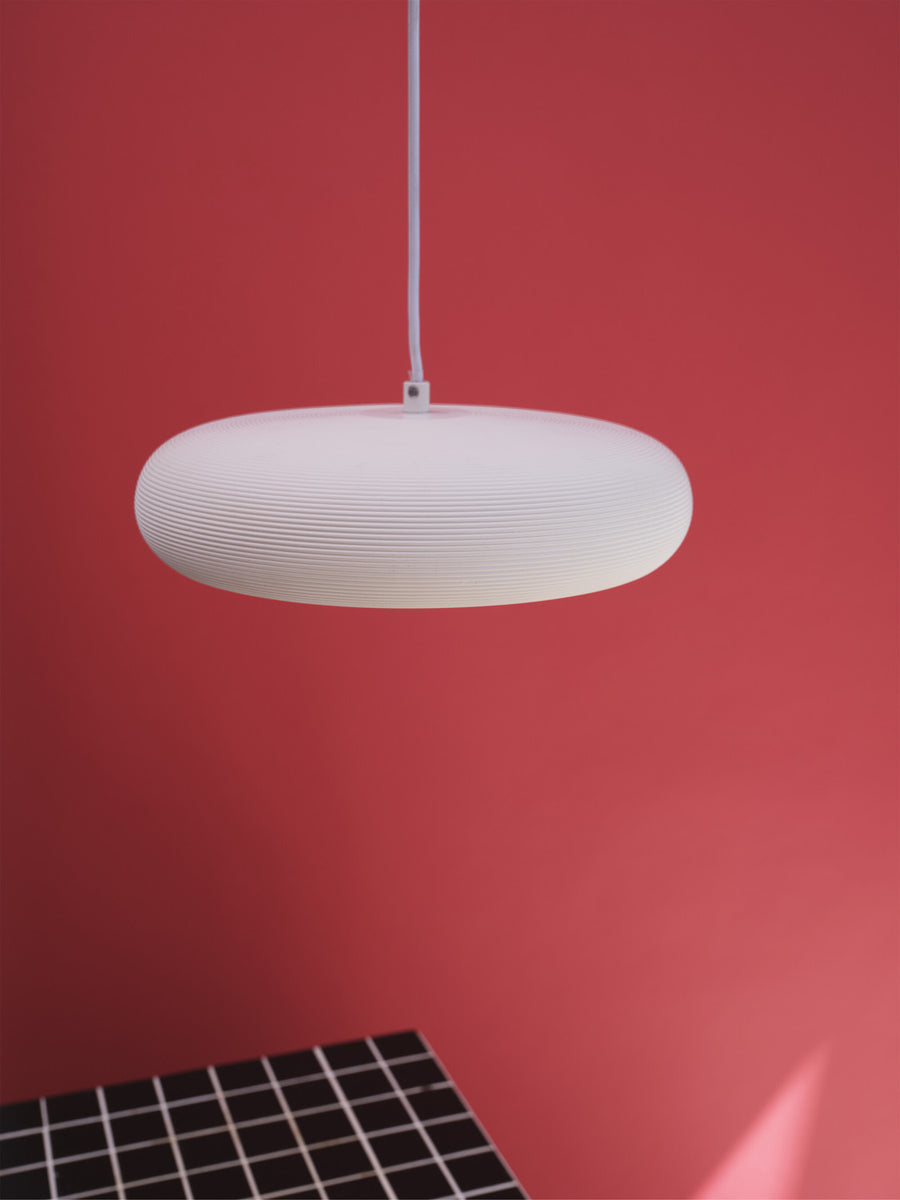 Gros plan sur la finition striée du diffuseur blanc, suspendu devant un mur rouge.