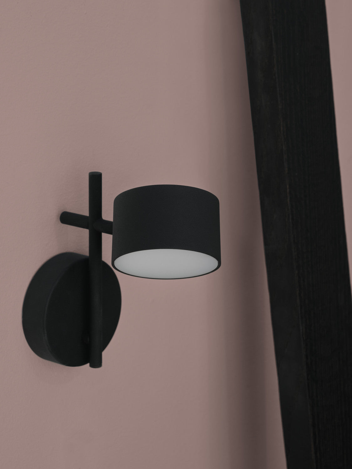 Vue rapprochée de l’applique noire fixée sur un mur rose, abat-jour cylindrique.