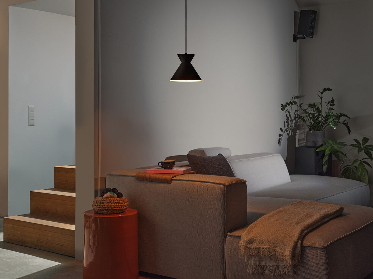 Mise en ambiance dans un salon moderne, suspension noire allumée au-dessus du canapé.