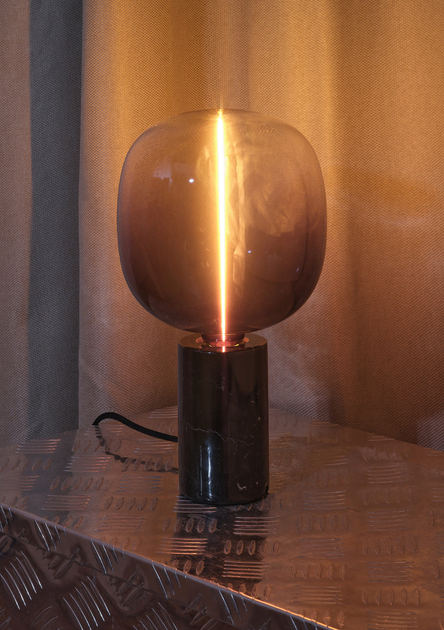 Gros plan de l’ampoule globe fumée allumée, filament lumineux sur surface métallique.