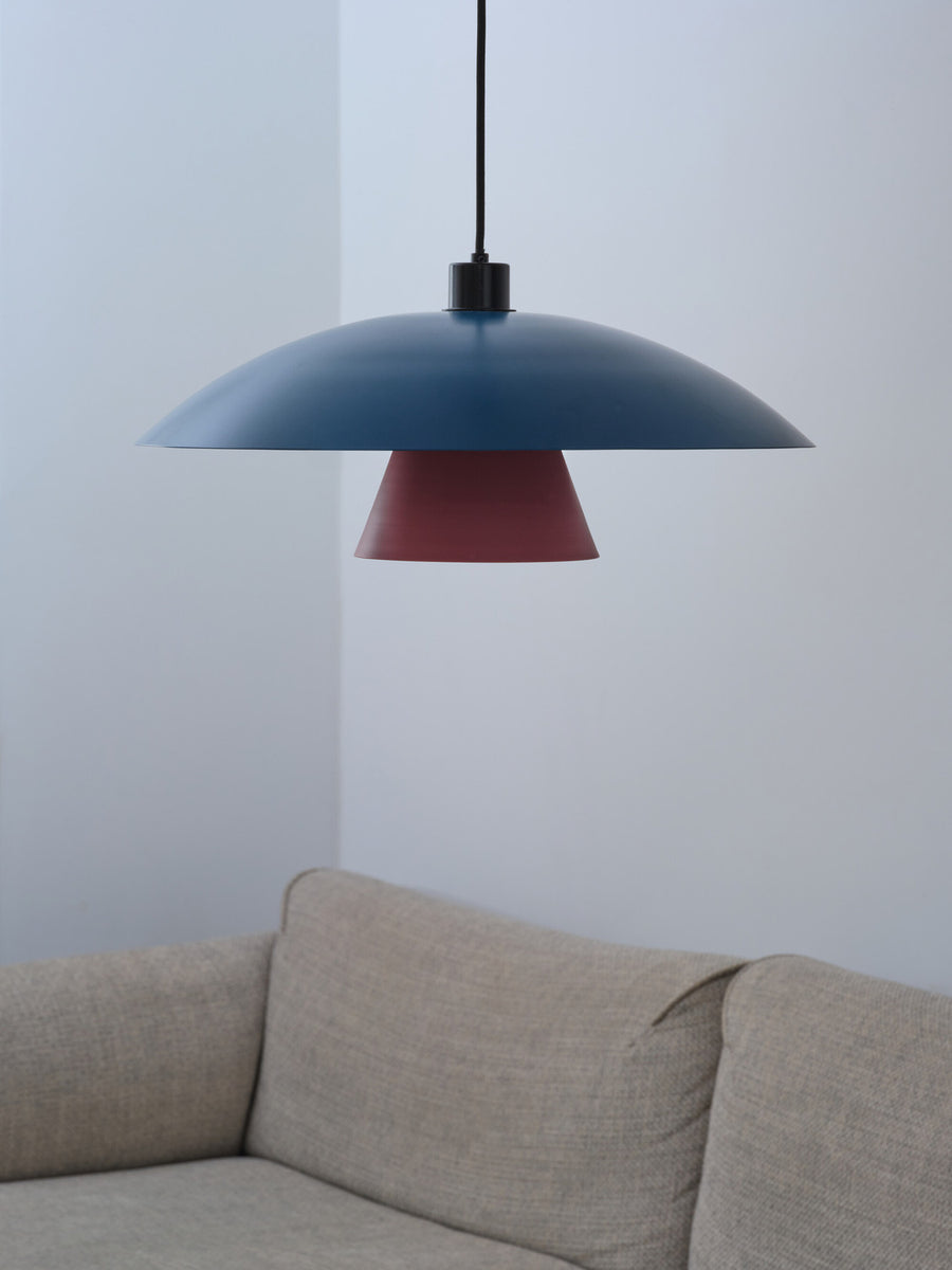 Gros plan de l'abat-jour bleu et du cône fuchsia au-dessus d'un canapé clair.