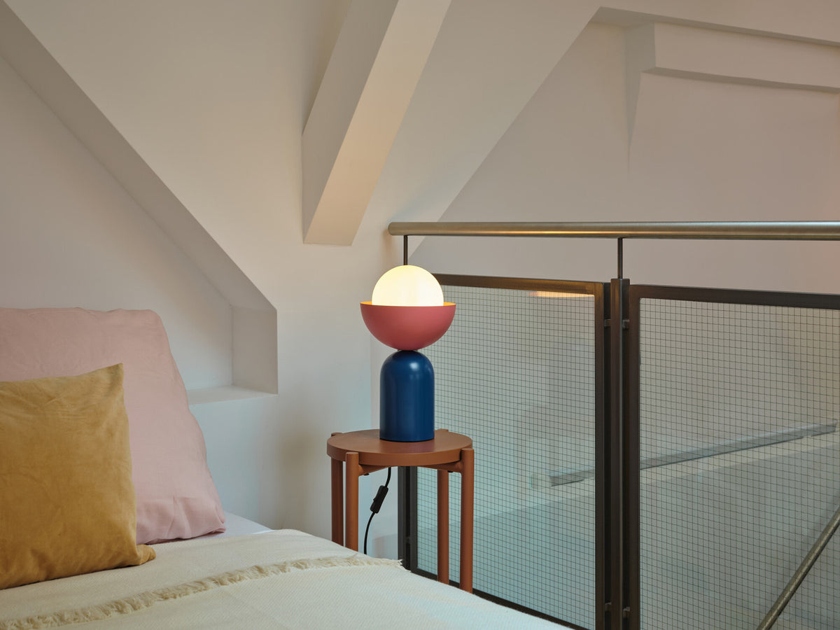 Lampe allumée posée sur une table d'appoint près d'un lit et d'une rambarde.