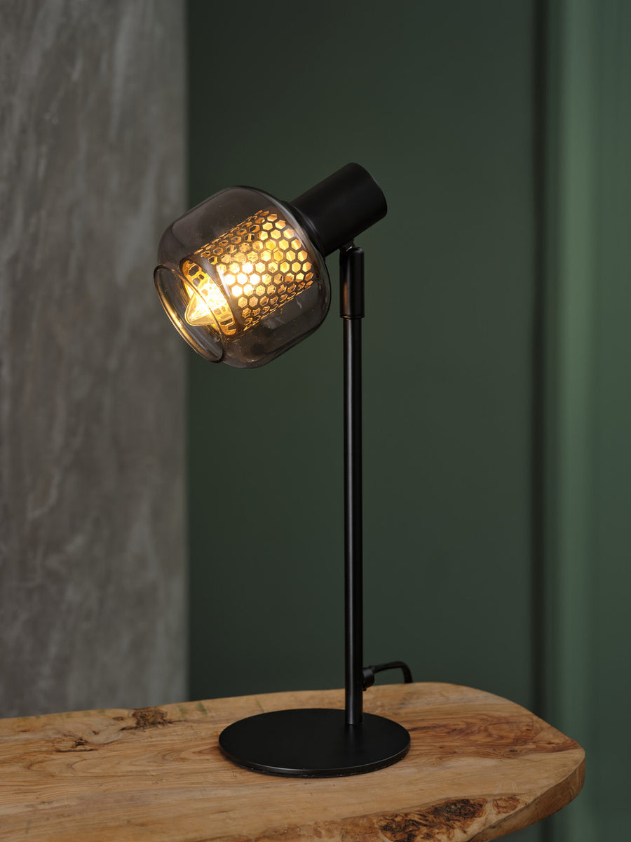 Lampe allumée posée sur une table en bois brut devant un mur vert