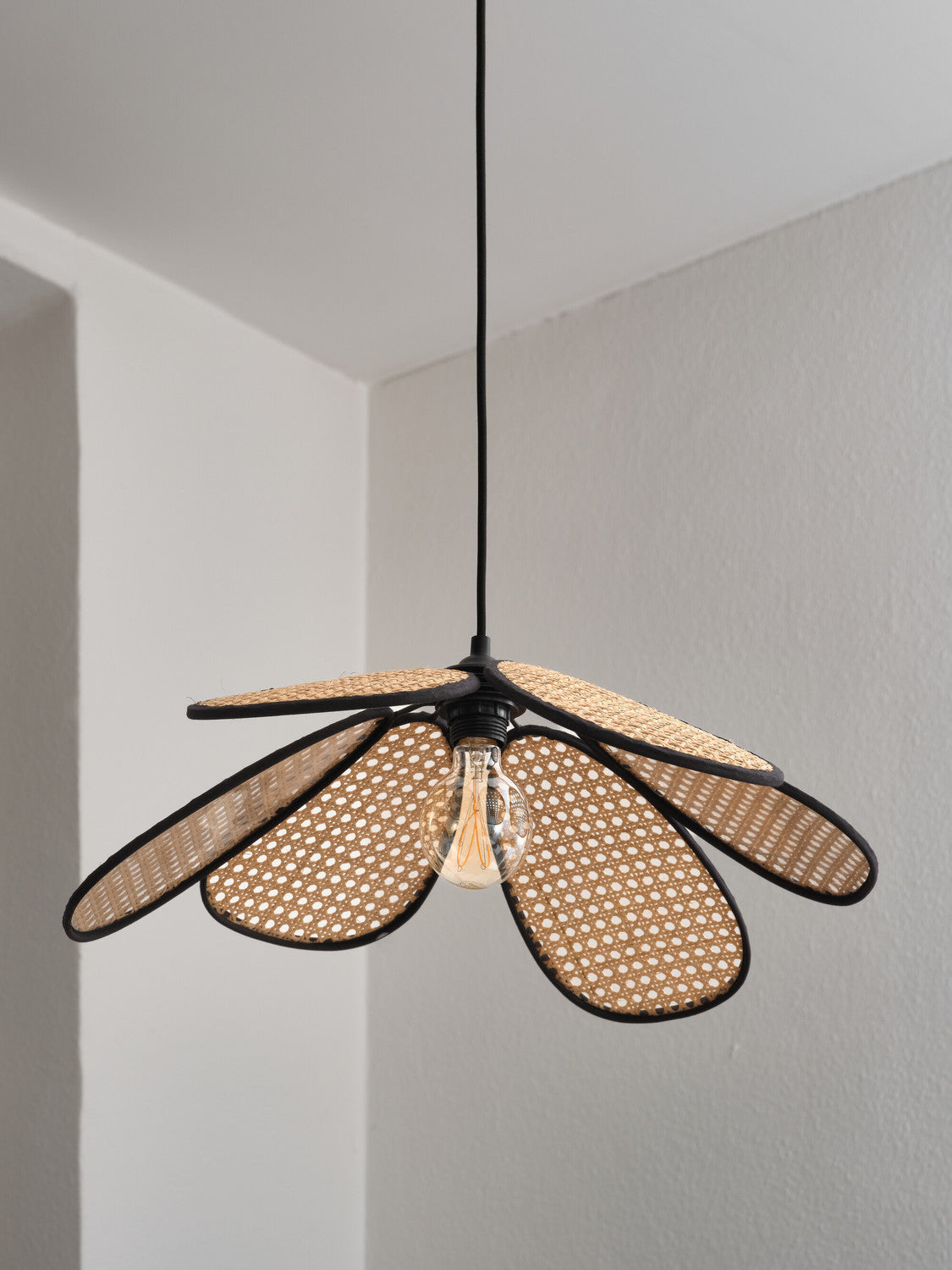 Détail rapproché de l'abat-jour en cannage et de l'ampoule Edison allumée.