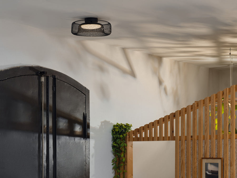 Plafonnier allumé au plafond, ombres en résille près d'une porte noire et de lattes bois.
