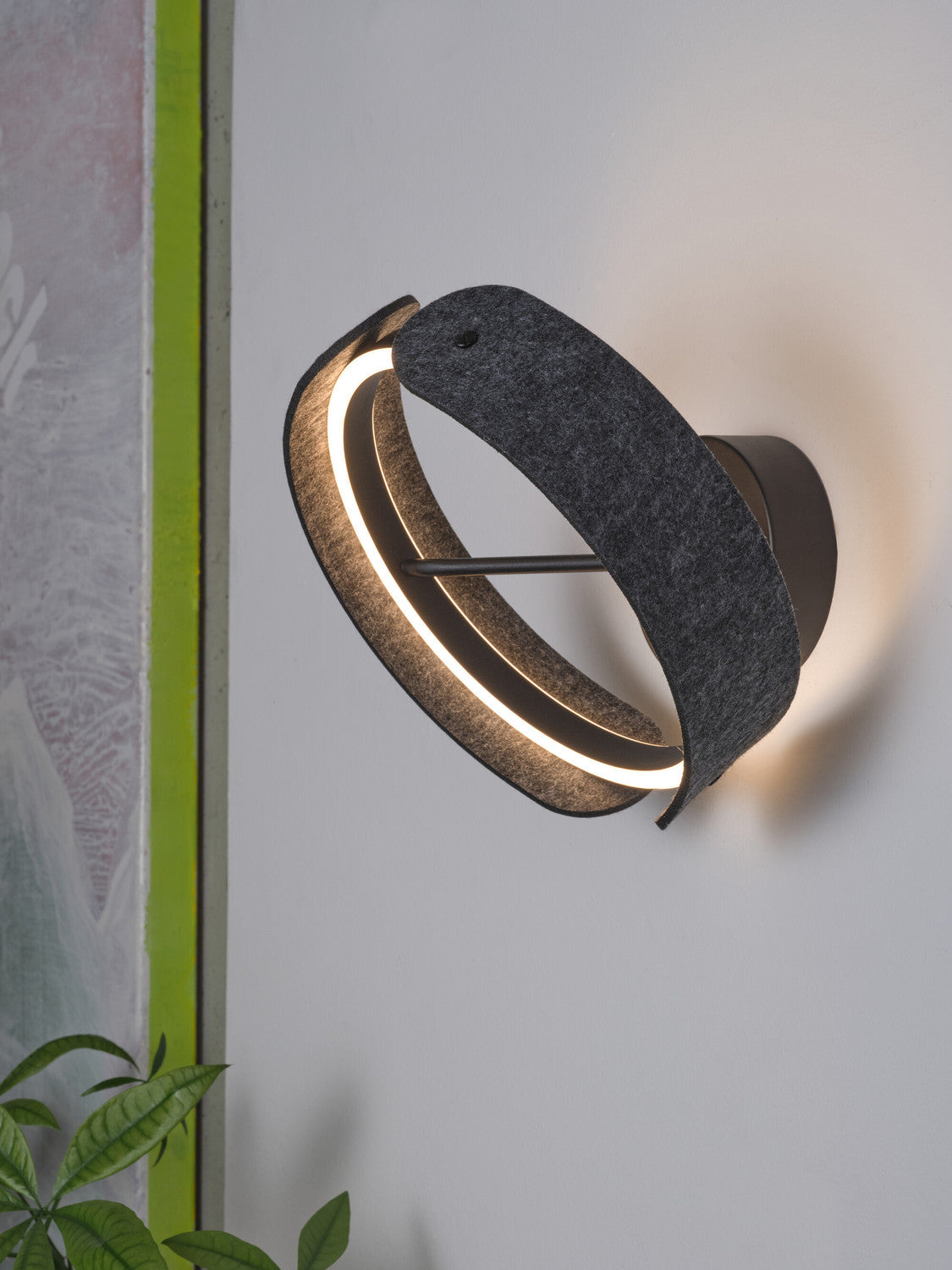 Vue latérale de l’applique allumée, halo lumineux et ruban de feutre anthracite.
