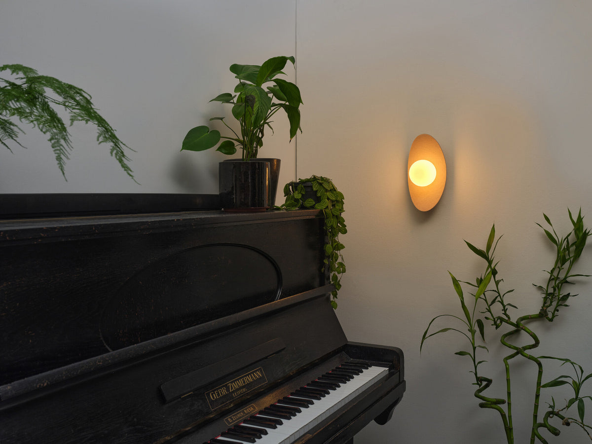 Applique murale allumée près d’un piano noir et de plantes vertes dans une pièce.