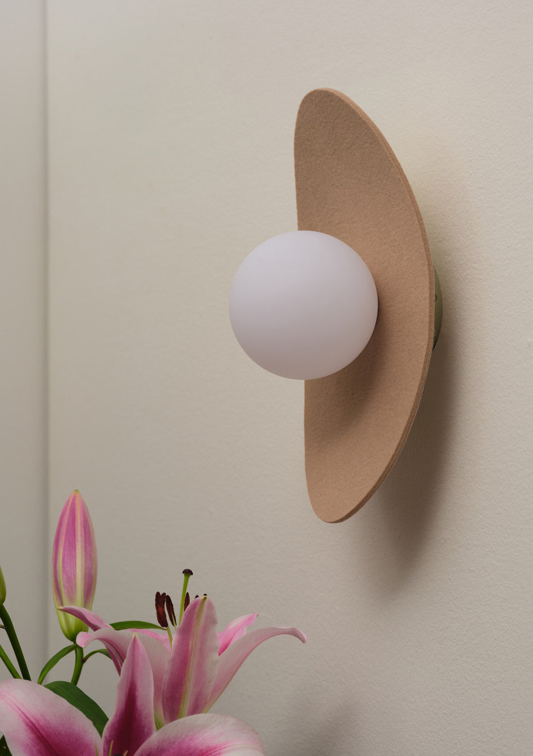 Vue rapprochée de l’applique ovale beige et de son globe blanc devant des lys.