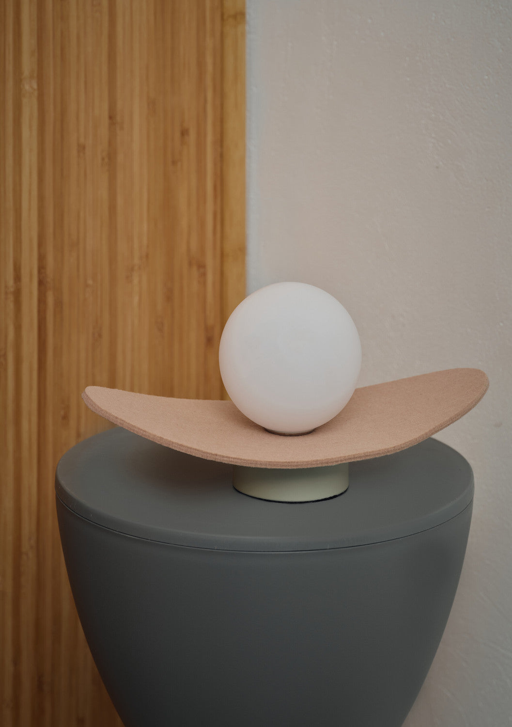 Lampe éteinte posée sur un tabouret gris, devant un panneau de bois vertical.