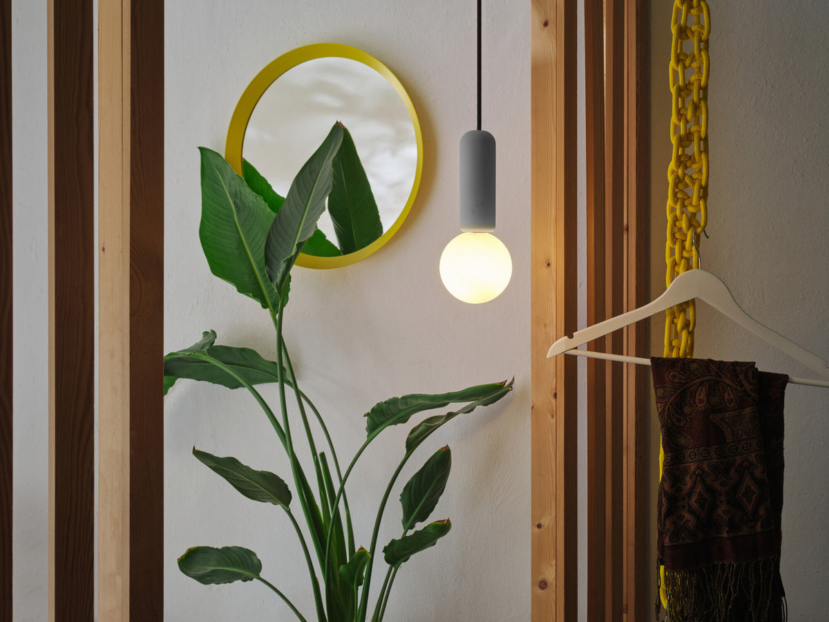Mise en ambiance dans une entrée avec miroir jaune, plante verte et vêtements suspendus.