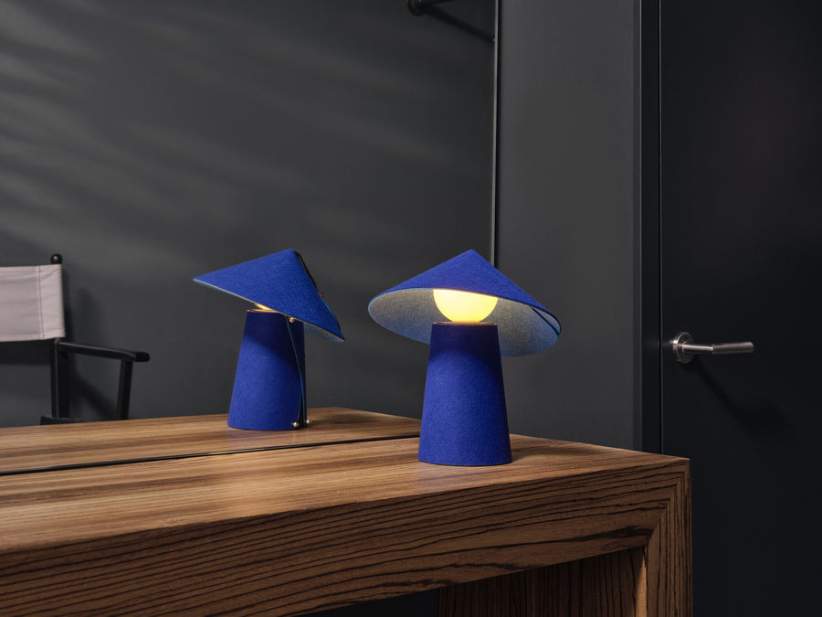 Deux lampes bleues en feutre sur un meuble en bois, éclairage chaud dans une pièce sombre.
