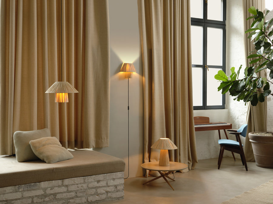 Scène de salon avec lampe à poser, suspension et applique en papier plissé.