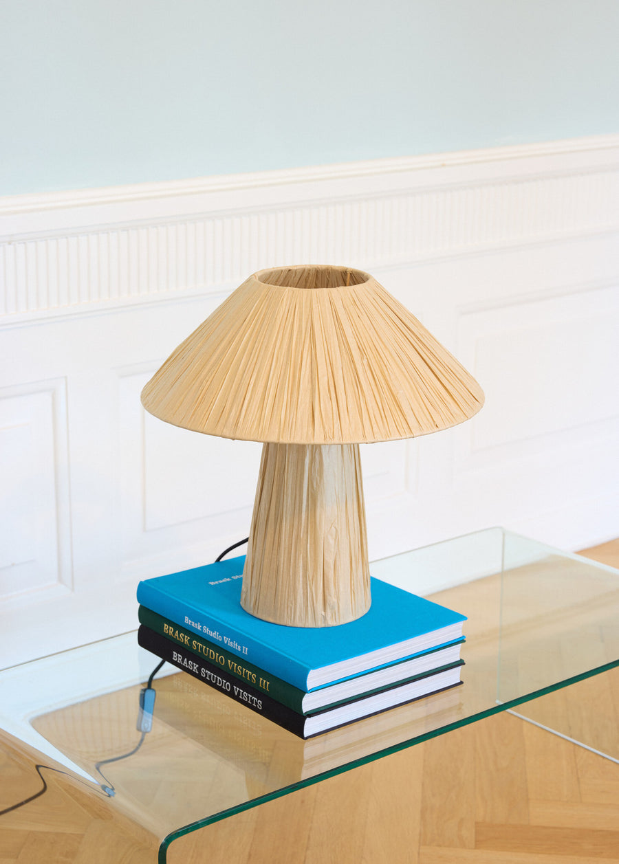 Lampe éteinte sur livres empilés, table vitrée et lambris mural clair.