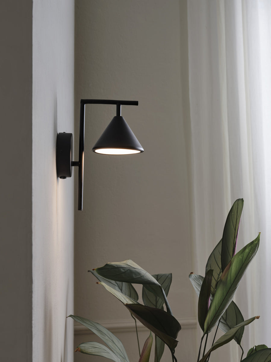 Applique noire fixée au mur près d'un rideau clair et d'une plante.