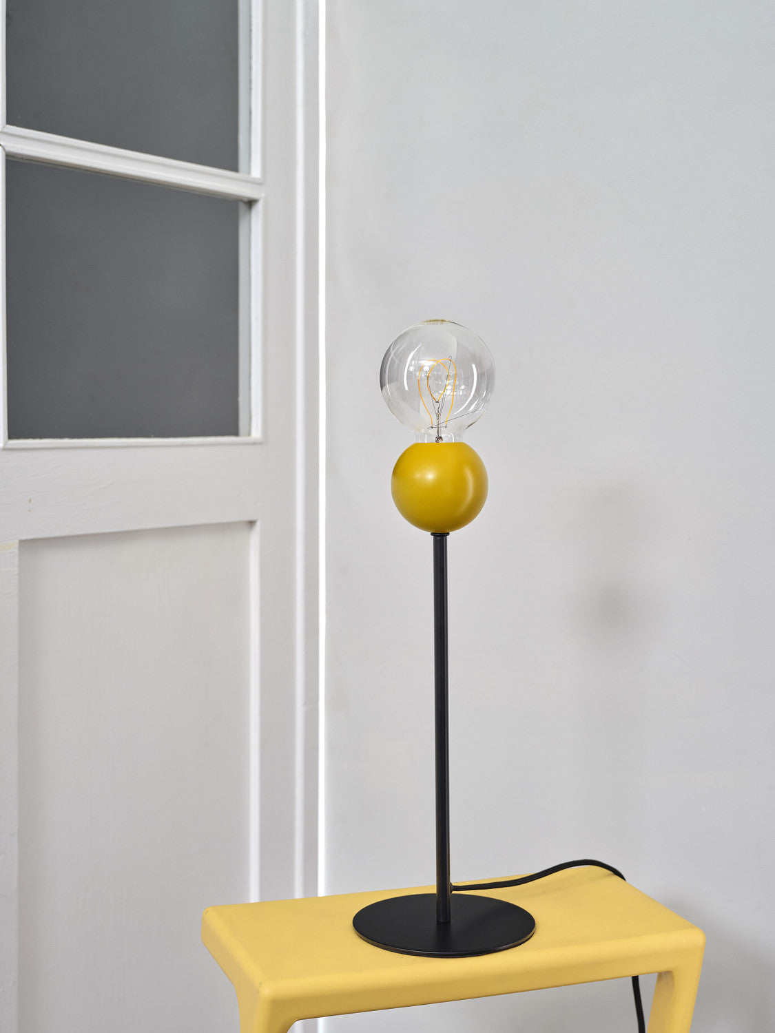 Lampe jaune posée sur un tabouret jaune devant une porte blanche