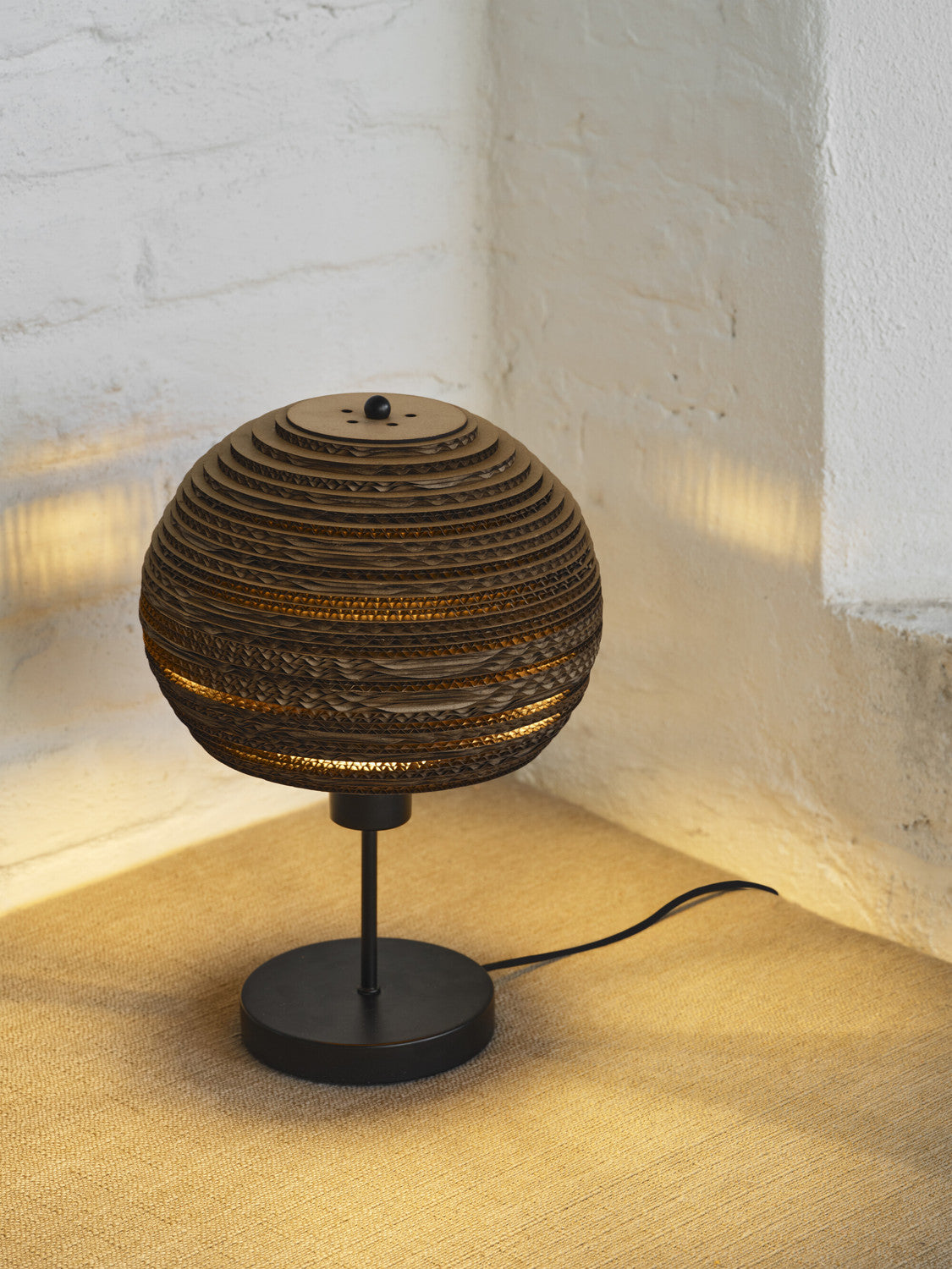 Lampe à poser éclairée sur une surface beige, motif ondulé du carton bien visible.