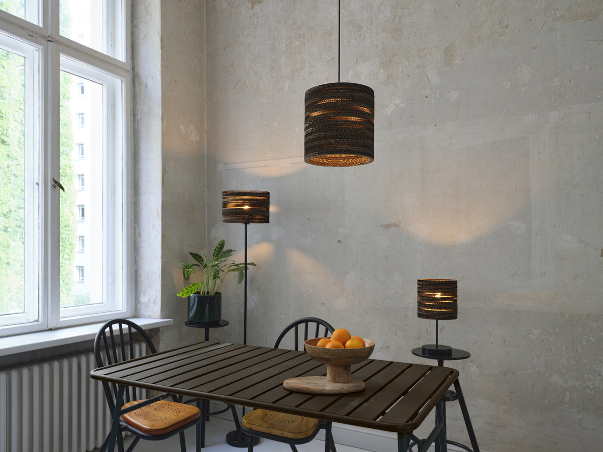 Scène de salle à manger avec suspension cylindrique en carton, lampadaire et lampe de table.
