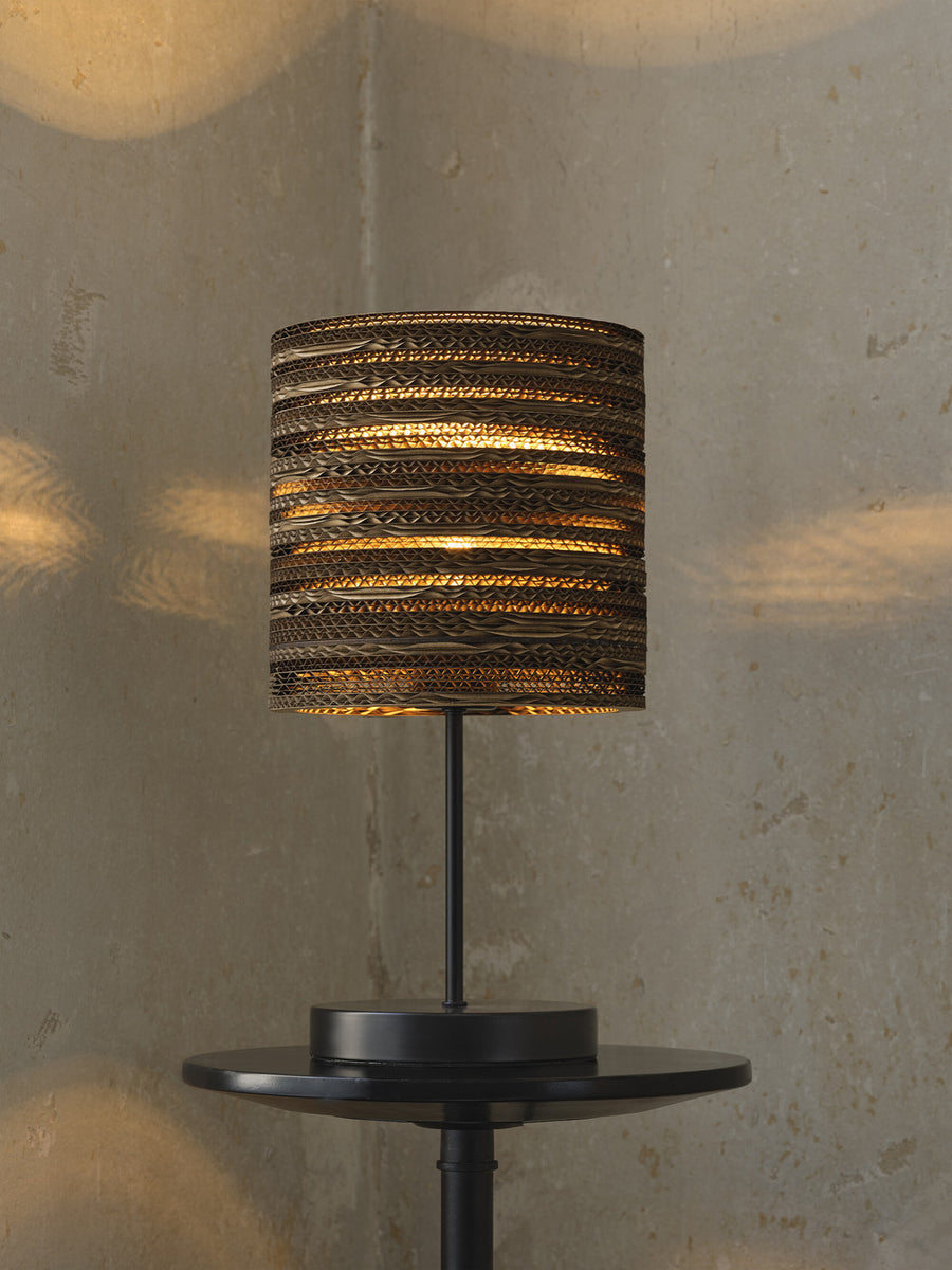 Lampe allumée en gros plan, abat-jour carton diffusant lumière chaude sur mur.