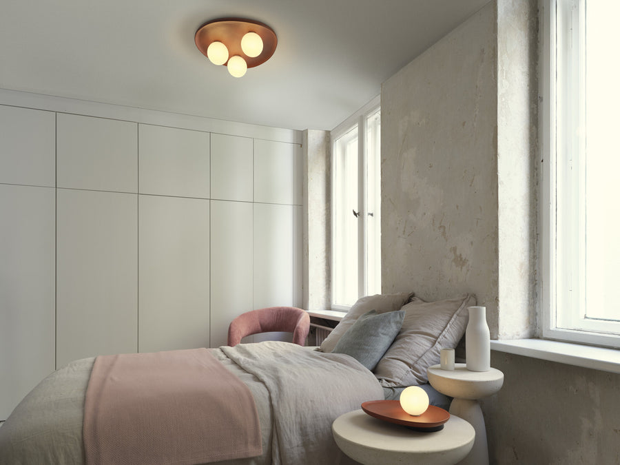 Chambre avec plafonnier terracotta et lampe de chevet allumée sur table blanche.
