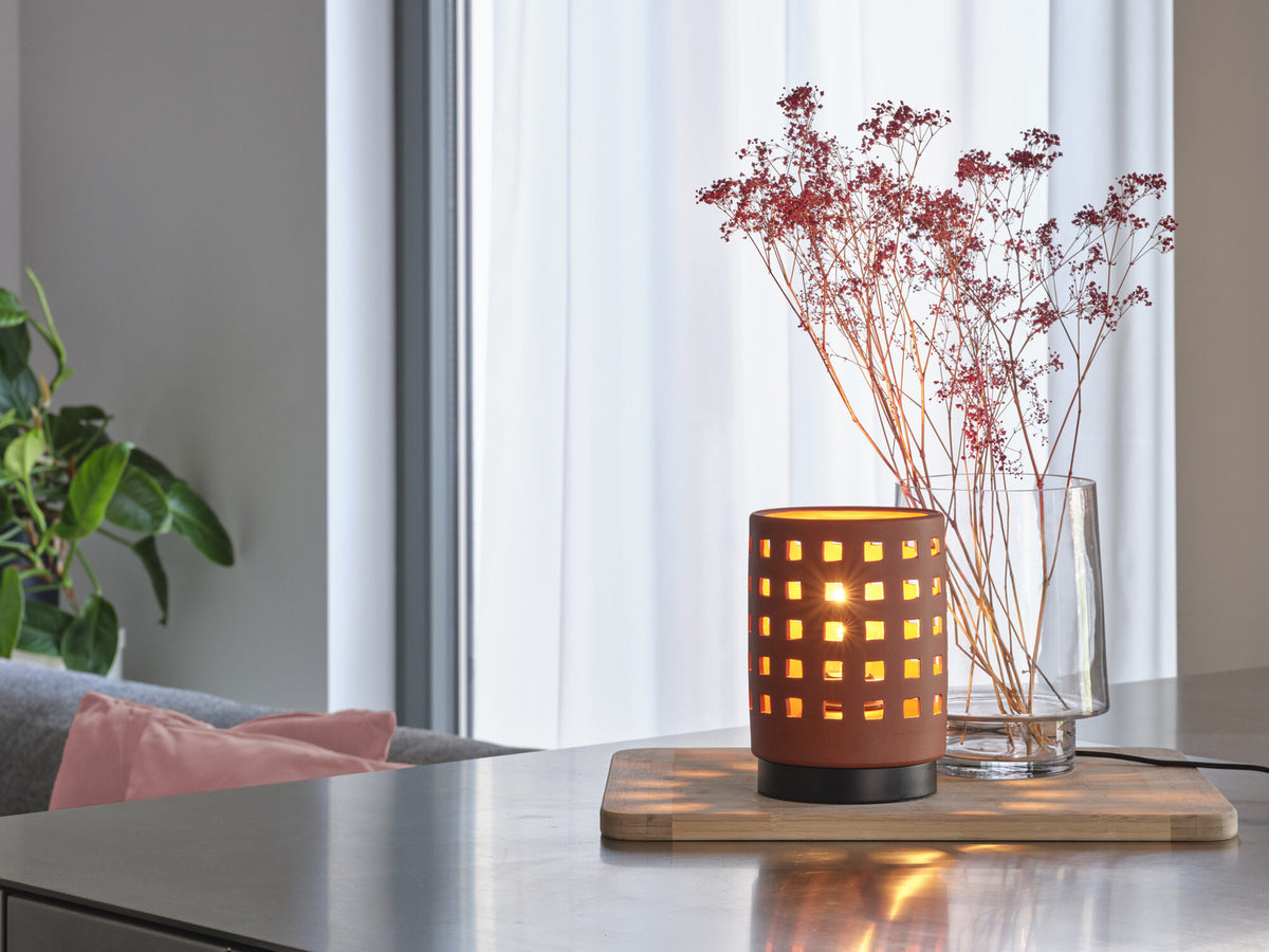 Mise en ambiance sur table en bois, lampe allumée près d’un vase de fleurs séchées.
