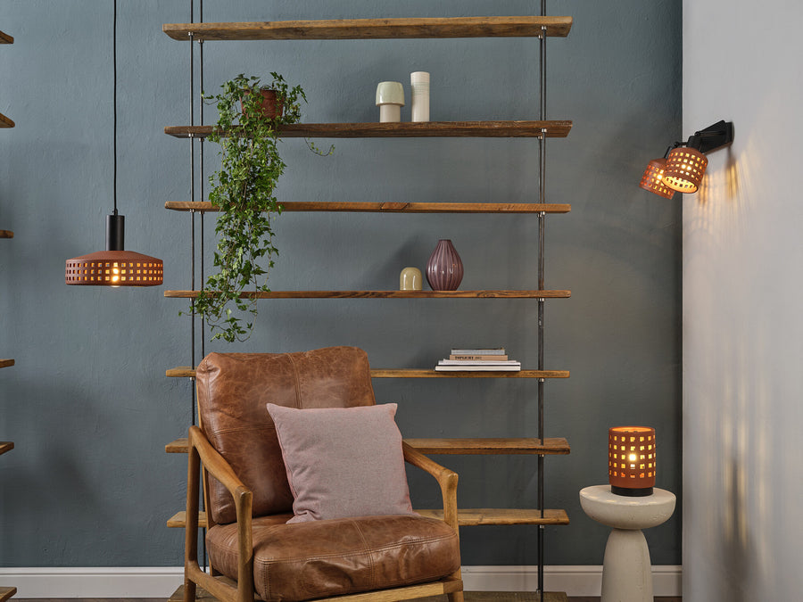 Scène de salon avec lampe à poser allumée sur un guéridon, étagères et fauteuil.