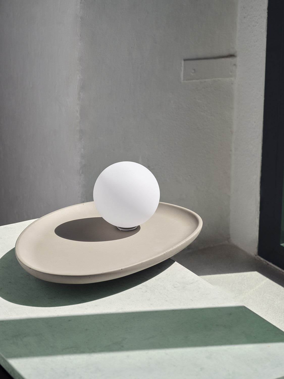 Lampe éteinte sur surface claire, ombre marquée du globe sur le plateau ovale.