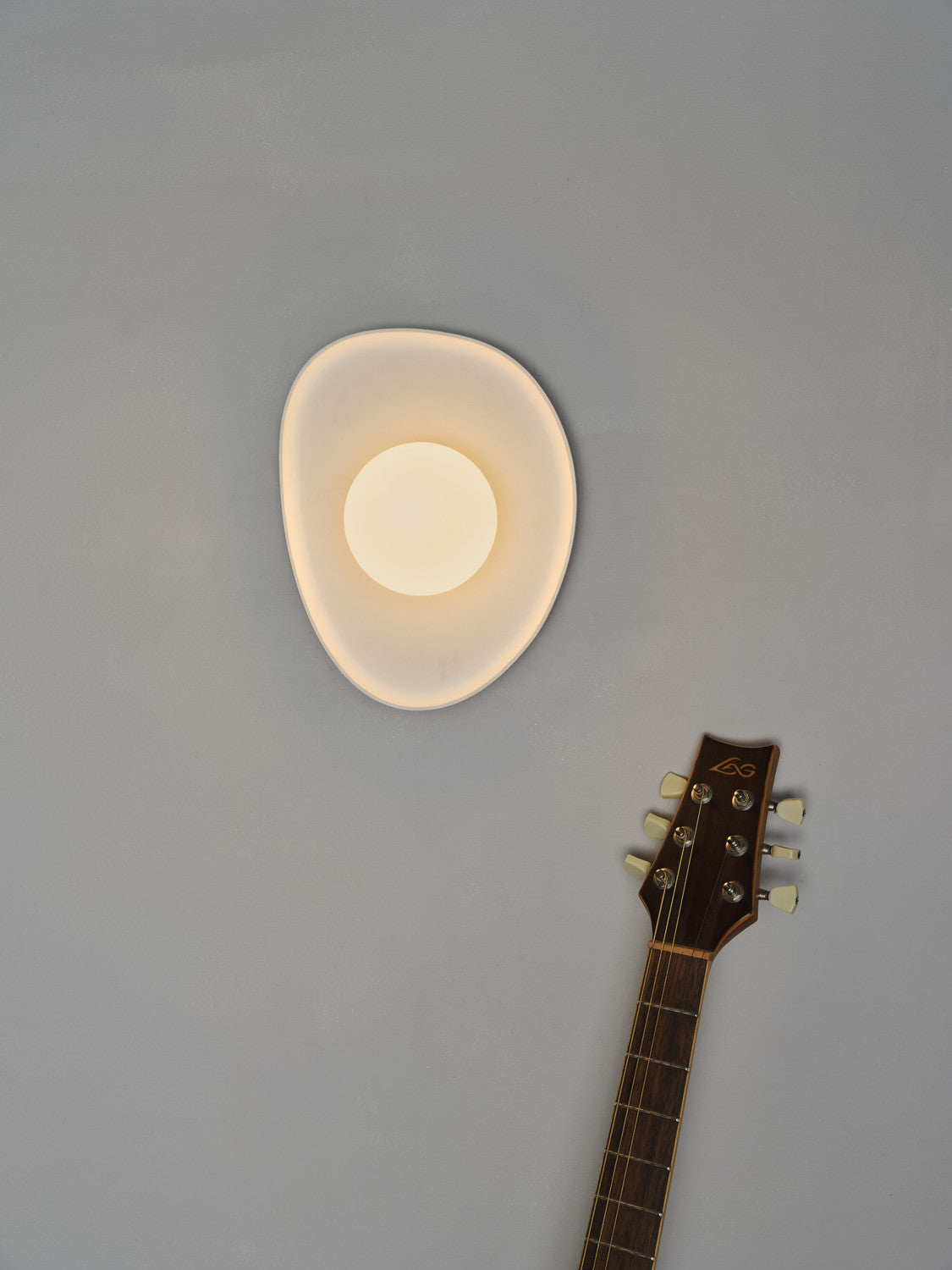 Vue rapprochée de l’applique allumée, halo lumineux et manche de guitare en bas.